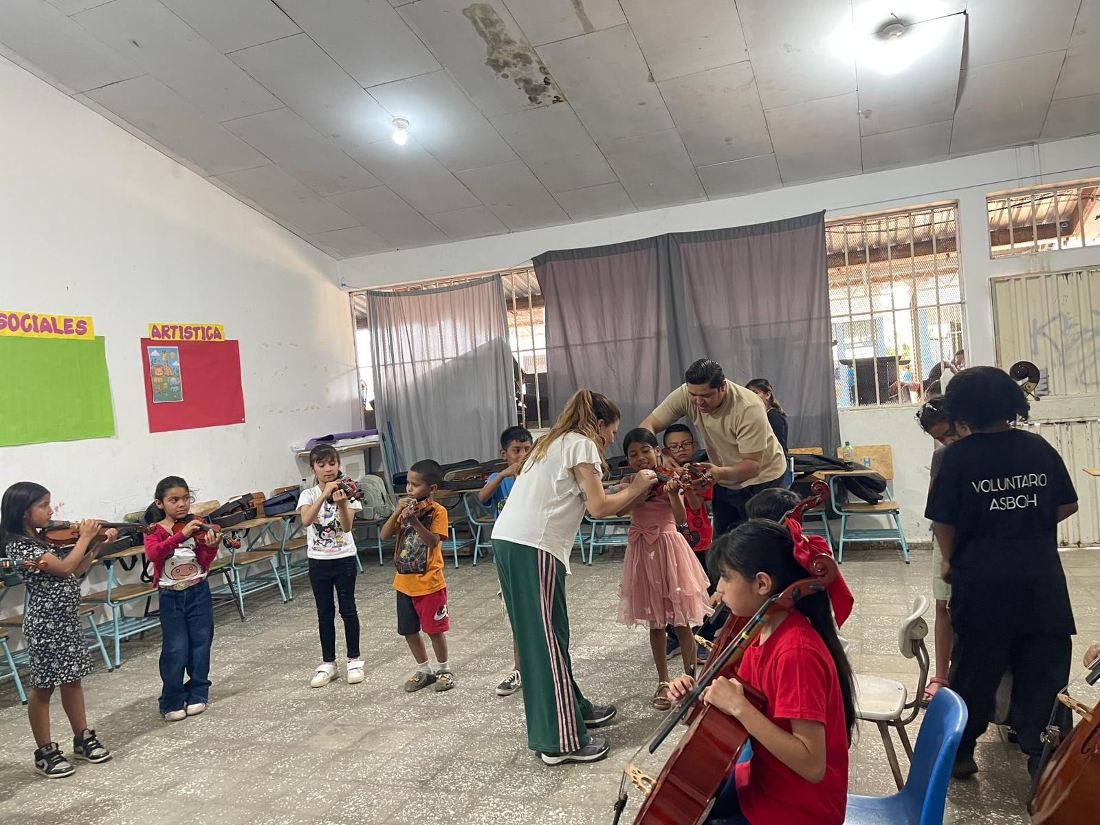 Clase de orquesta en el aula: niñas y niños tocan violín y violonchelo con la guía de adultos