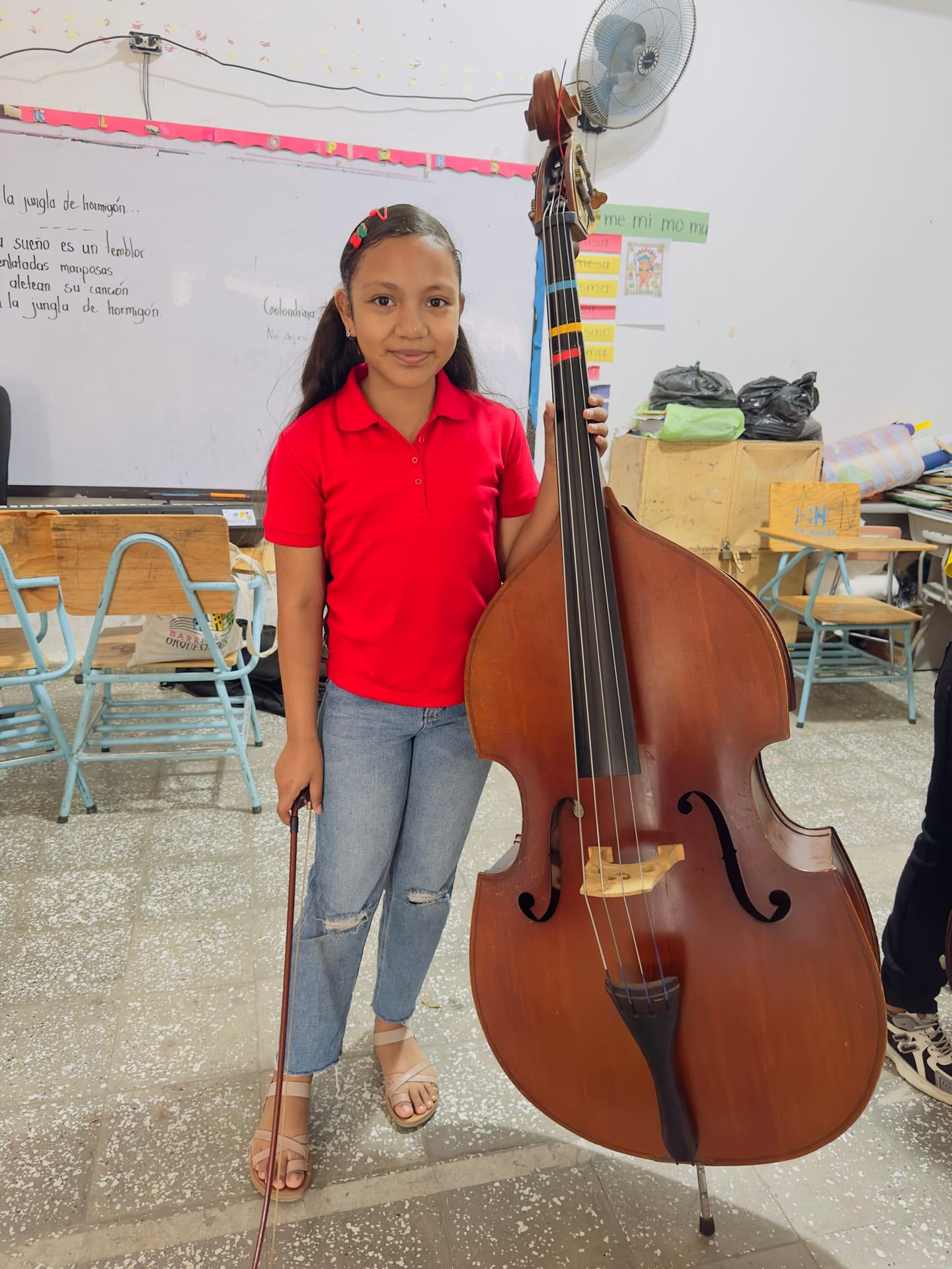 Una niña sonríe junto a su contrabajo, con el arco en la mano