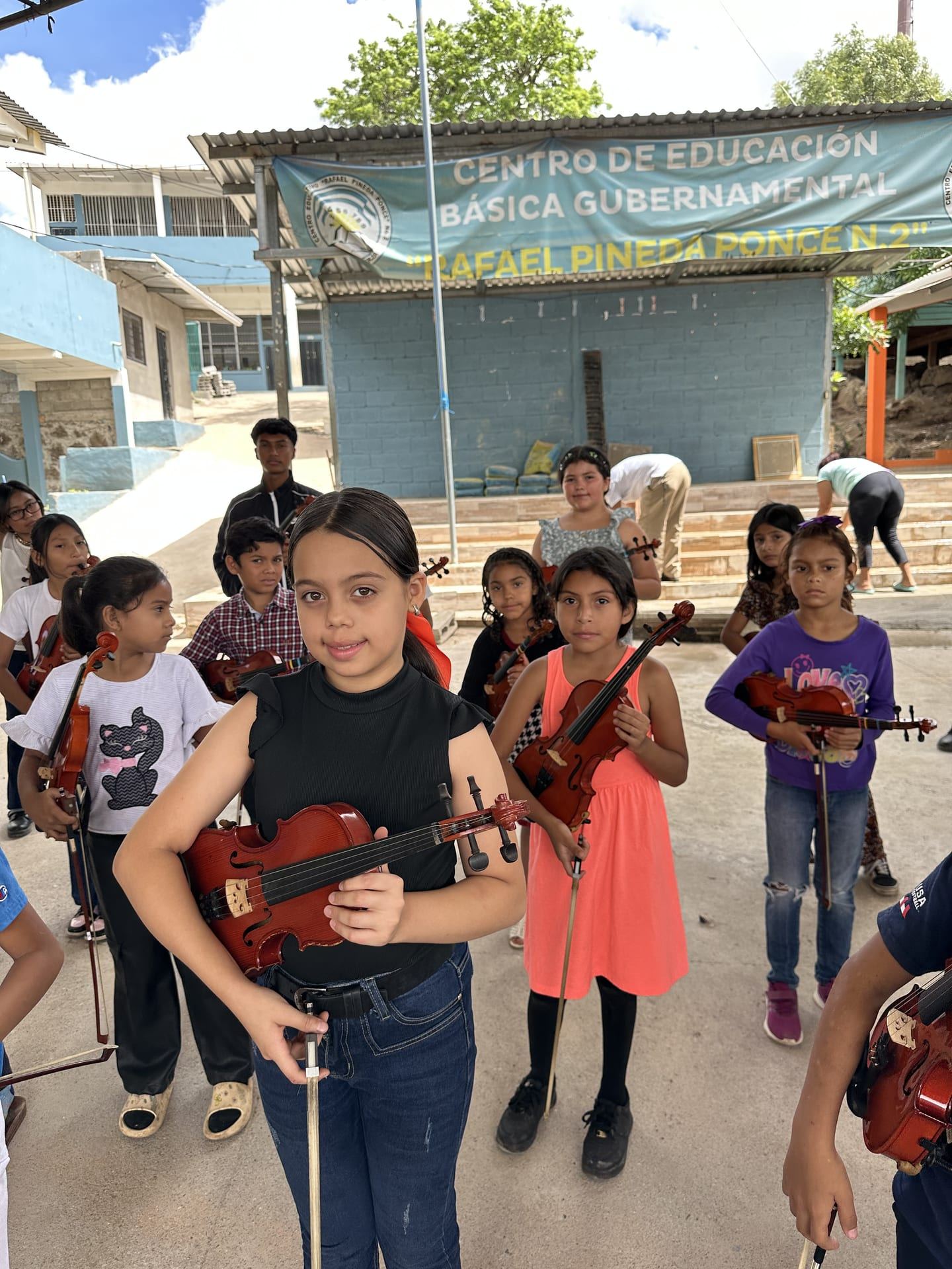 Una niña sostiene su violín entre otros alumnos, en el patio del centro educativo