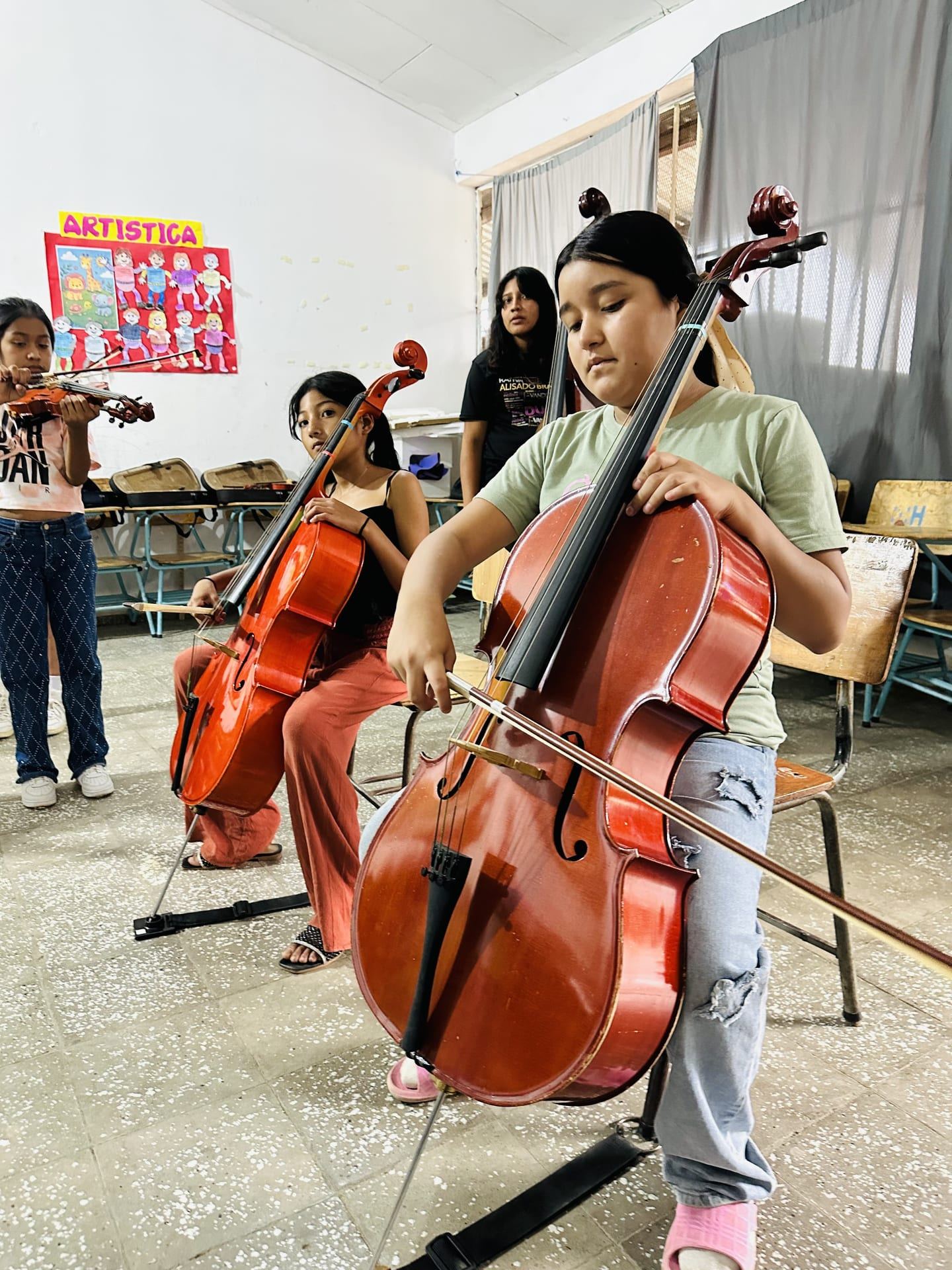Una niña toca el violonchelo en el aula, junto a otras alumnas que ensayan