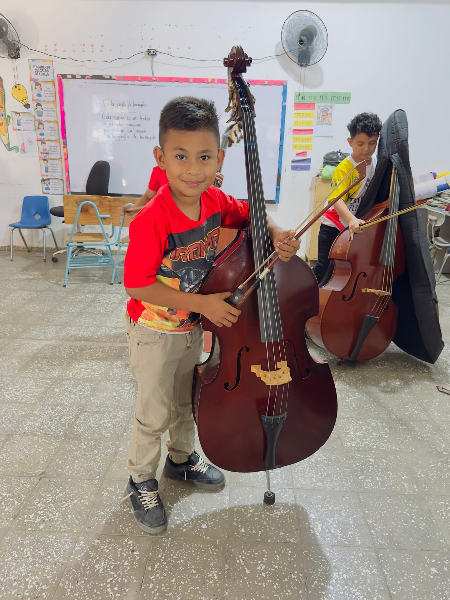 Un niño sostiene con una sonrisa un contrabajo casi de su tamaño