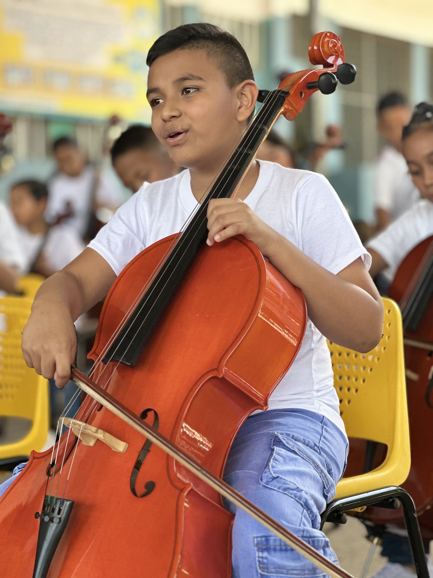 Un niño toca el violonchelo durante el concierto del 18 de junio de 2026, con otros alumnos desenfocados al fondo