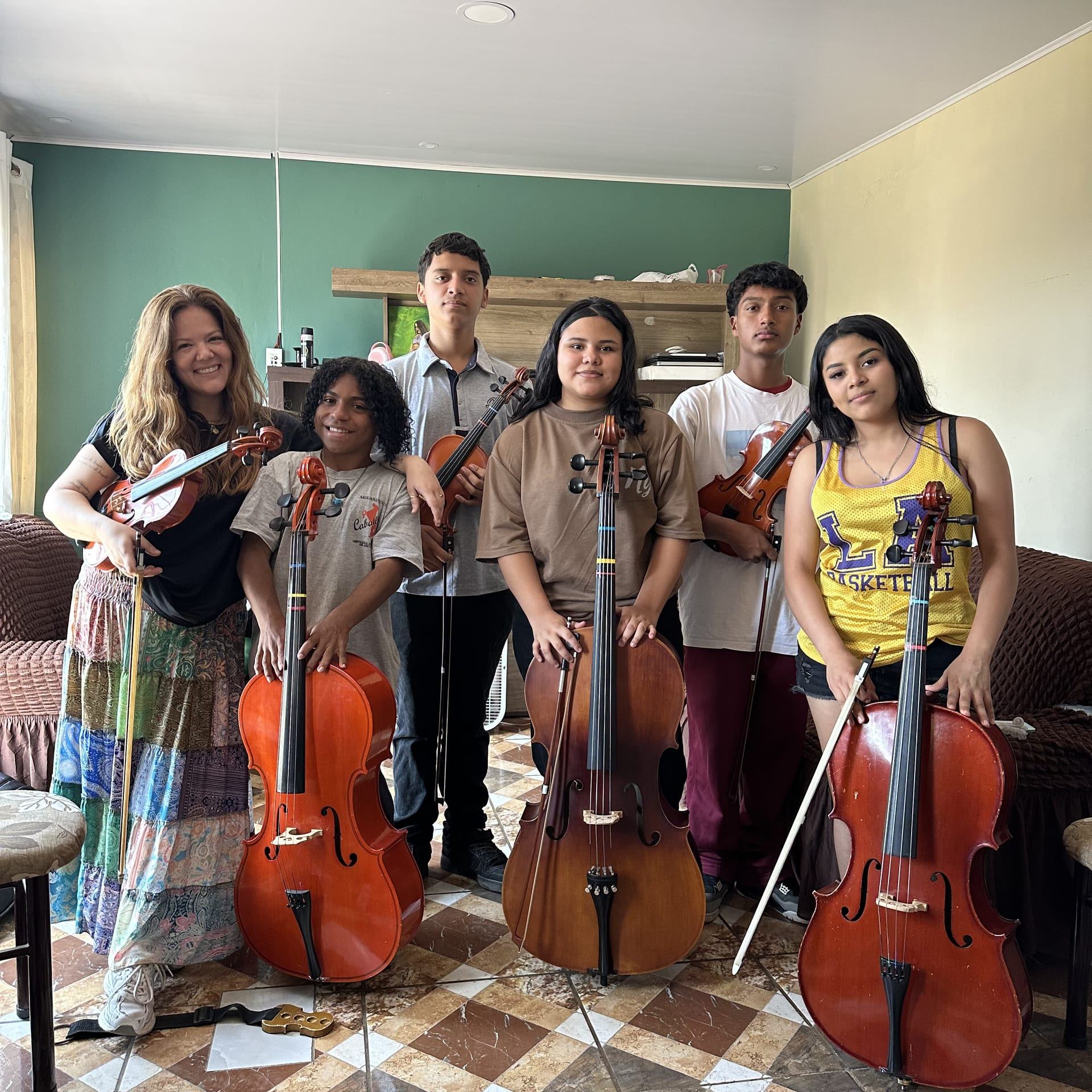 Cinco jóvenes con sus violonchelos y violines posan junto a una mujer adulta, que también sostiene su violín